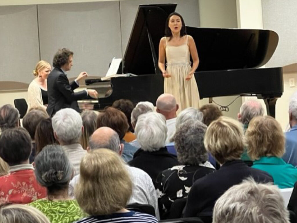 A woman in white dress standing next to a piano.