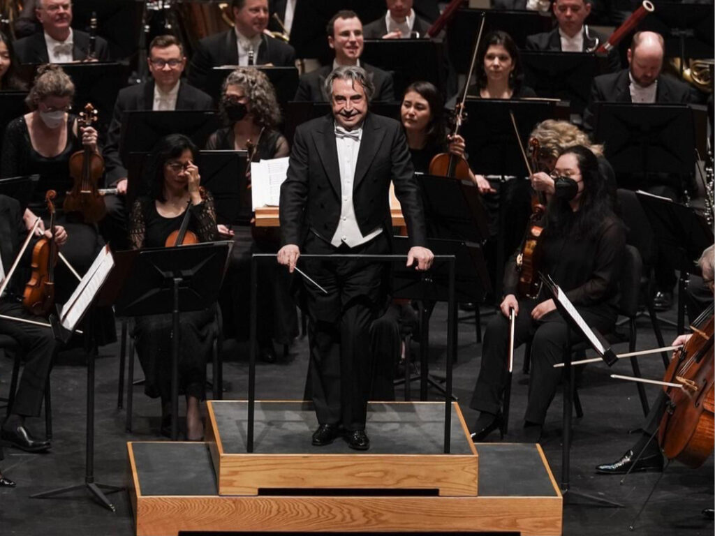 A man standing on top of a stage with orchestra members behind him.