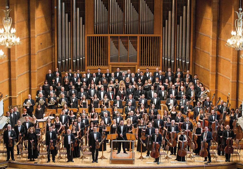 A large orchestra is standing in front of the stage.